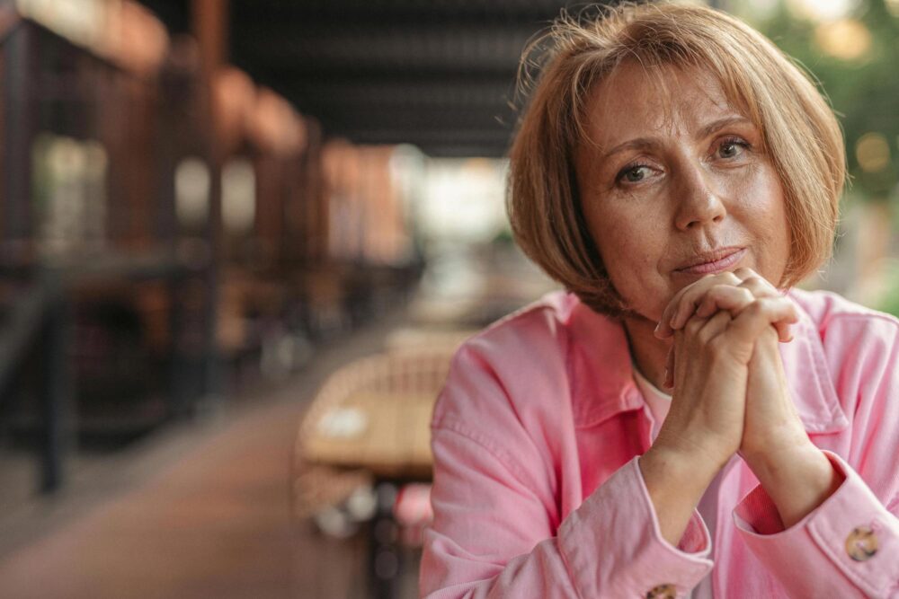 A woman wearing pink, looking into the camera with her hands folder.